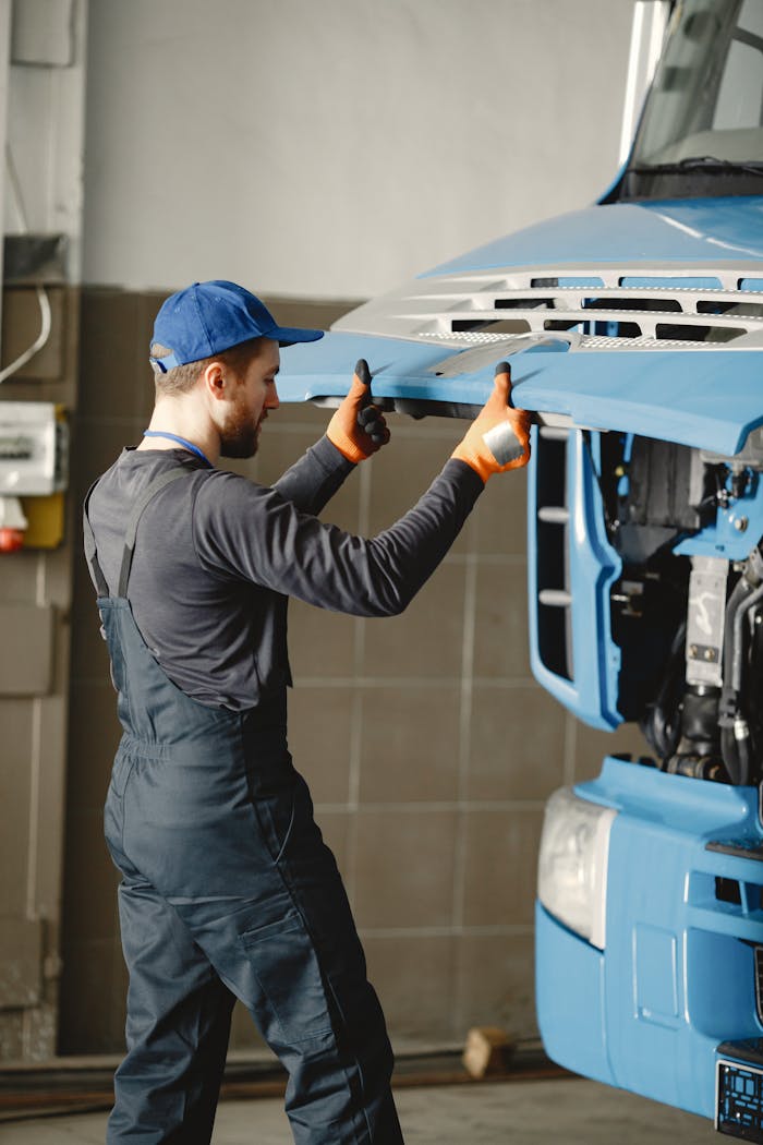 Man in Work Clothes and Blue Cap Opening Front Mask of Blue Truck